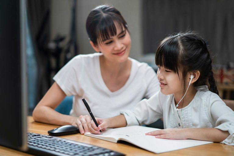 Homeschool Asian little young girl learning online class from school teacher with help from mother